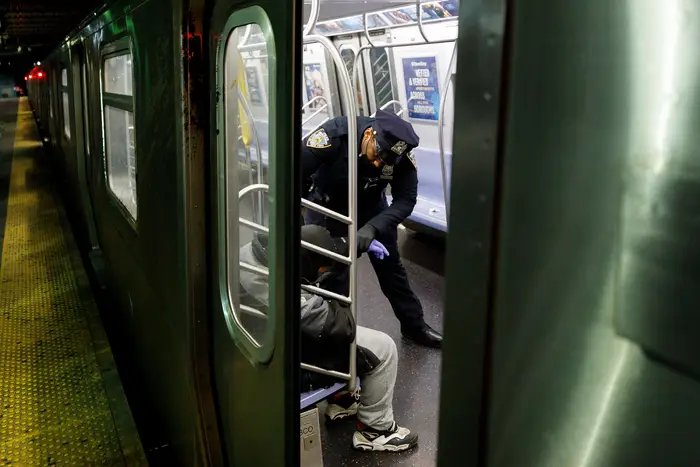 A New York City police officer asks a sleeping man to exit a train as part of the suspension of service for the night at the Coney Island station, May 6, 2020.